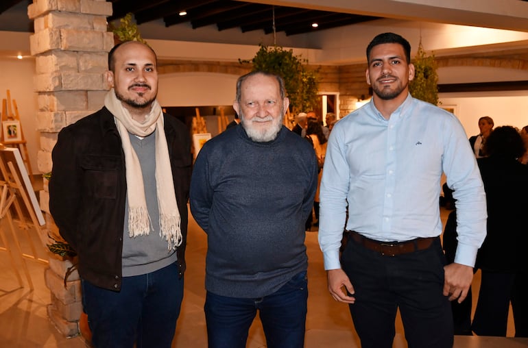 Hombre mayor con suéter gris oscuro y dos jóvenes en chaquetas oscuras, posando en un interior moderno rodeado de plantas.