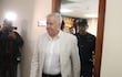 Jorge Brítez, vestido con traje claro y una camisa blanca, camina hacia una oficina junto a un agente de seguridad uniformado.