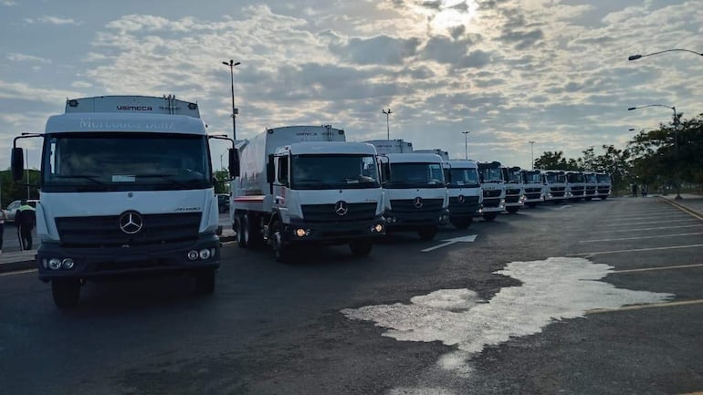 Fila de camiones Mercedes Benz en área pavimentada, logotipo 'Usimeca' visible en uno, bajo cielo parcialmente nublado.