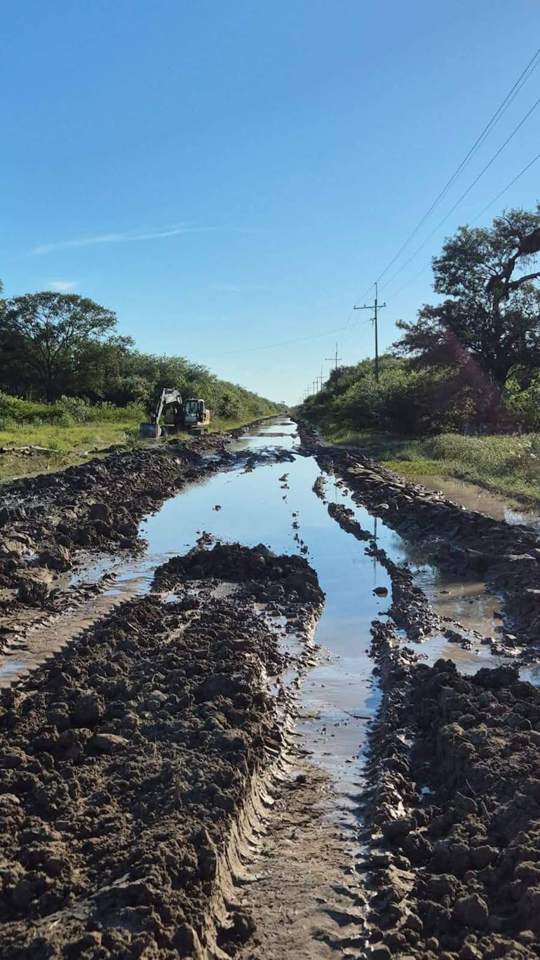 Maquinaria pesada en camino rural de tierra maltratado, rodeado de vegetación densa y cielo despejado.