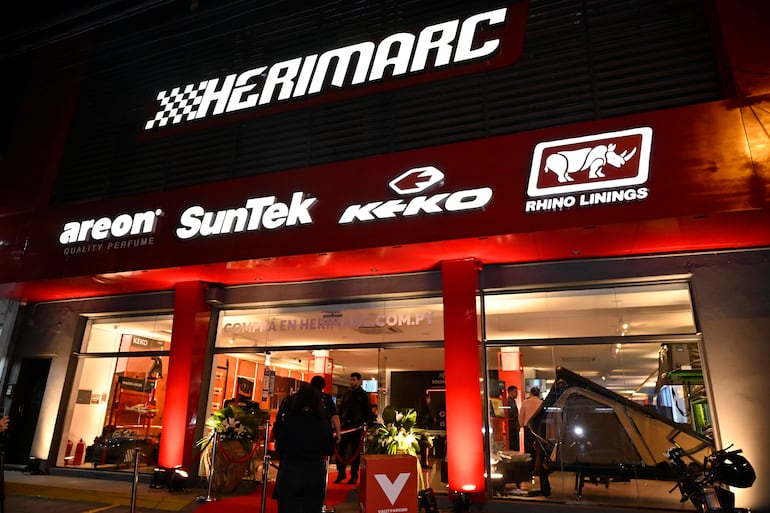 Fachada de Herimarc iluminada, con alfombra roja y letreros de marcas como Areon y Keko, sin personas visibles.