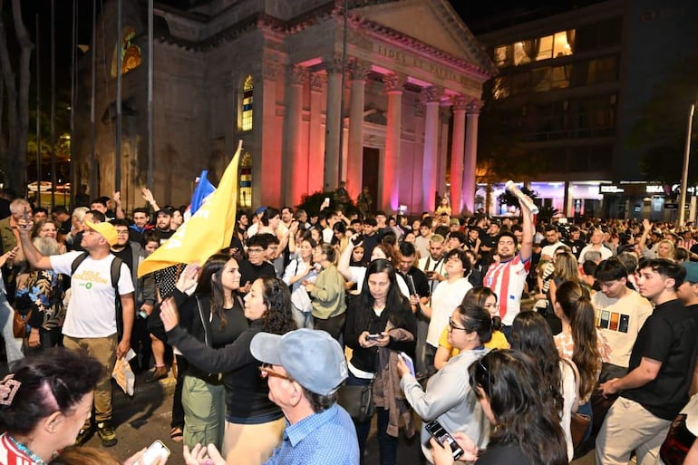 Hombres y mujeres enérgicos sostienen una bandera amarilla, con un letrero que dice 'FIDES ET PATRIA' visible detrás.