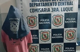 Joven con capucha y camiseta rosa de espaldas en comisaría, rodeado de decoración institucional de Policía Nacional.