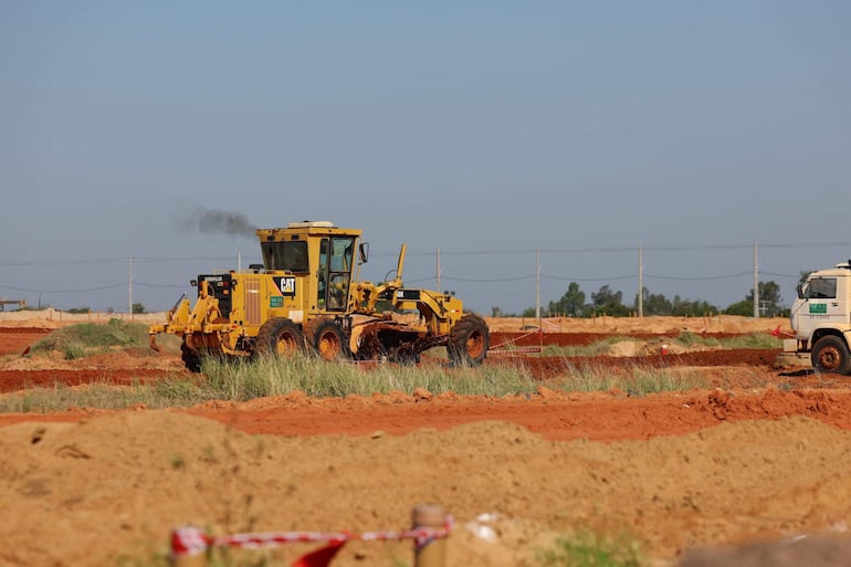 Equipo de construcción en obra con máquina amarilla Caterpillar y camión blanco en terreno rojizo bajo un cielo despejado.