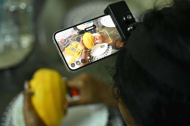 Esta fotografía, tomada el 15 de mayo de 2026, muestra a la ama de casa india Nagireddy Sriramyachandra llevando un teléfono inteligente en la cabeza mientras registra sus movimientos mediante captura de movimiento al cortar mangos en su hogar en Chennai.