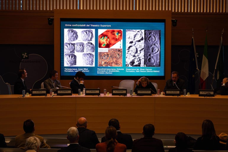 El paleontólogo del Museo de Historia Natural de Milán, Cristiano Dal Sasso (der.), comenta fotografías proyectadas en una pantalla durante una conferencia de prensa para presentar el descubrimiento de miles de huellas de dinosaurios halladas en el Parque Nacional del Stelvio, en Italia, cerca de las zonas que albergarán los Juegos Olímpicos de Milán-Cortina 2026, en Milán, el 16 de diciembre de 2025.