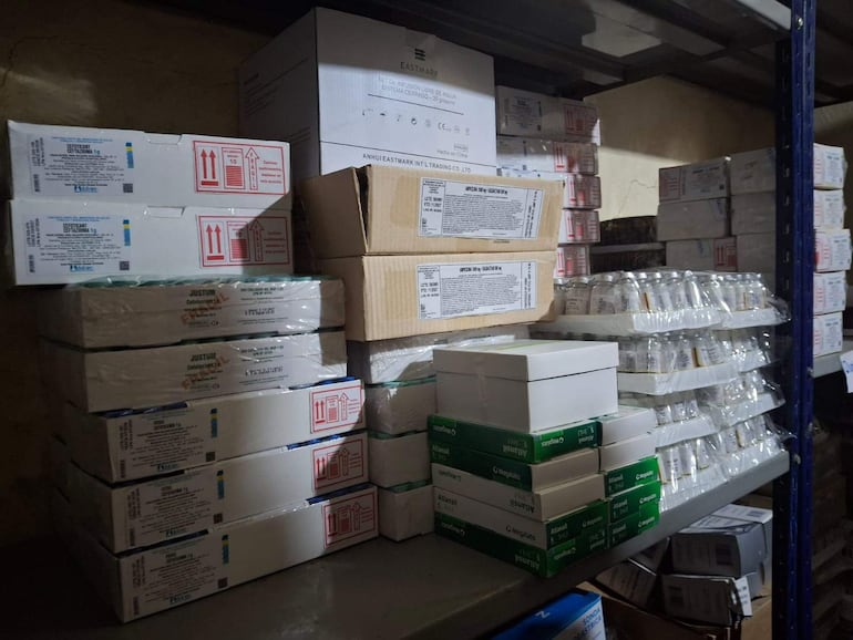 Cajas apiladas de medicamentos y suministros médicos en un almacén organizado y poco iluminado.