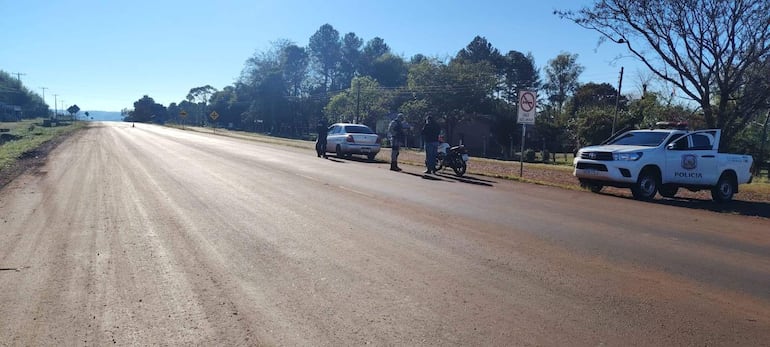 Tres policías conversan al lado de un coche blanco, mientras un civil en motocicleta dialoga con ellos en una carretera rural.