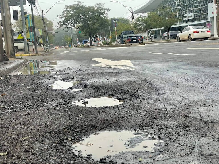 Calle de Asunción con pavimento en mal estado, baches con agua y vehículos circulando en un entorno nublado.