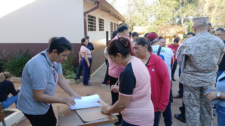 Mujeres en camiseta gris y rosa revisan documentos al aire libre, rodeadas de un grupo de personas en espera como parte de la manifestación.