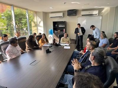 Emiliano Fernández con suéter claro habla en una reunión con 12 personas escuchando atentamente en una sala luminosa.