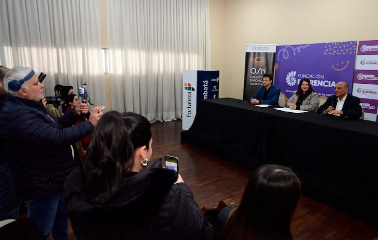María Victoria Sosa en el centro, vestida con abrigo claro, mientras dos hombres la escuchan en un ambiente formal.