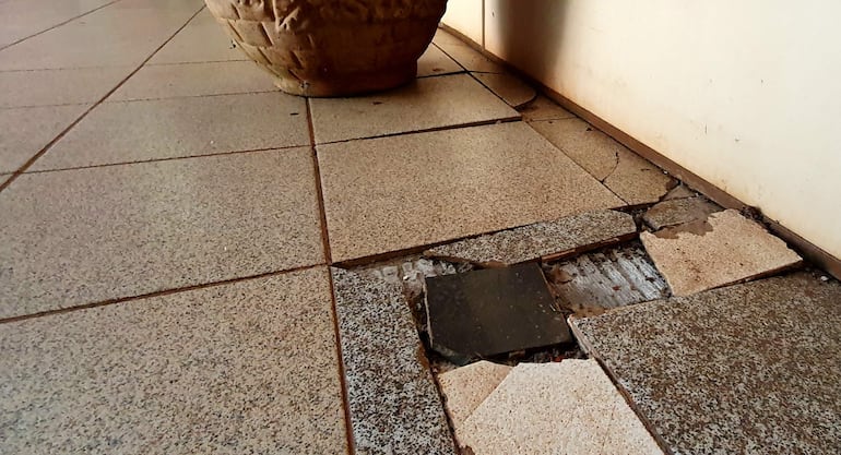 Piso dañado en Fiscalía, con baldosas rotas y una maceta clásica en un espacio descuidado.