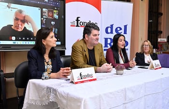 Cuatro personas sentadas en mesa. Dos mujeres, una de cabello oscuro y otra rubia con gafas, participan en una discusión formal.