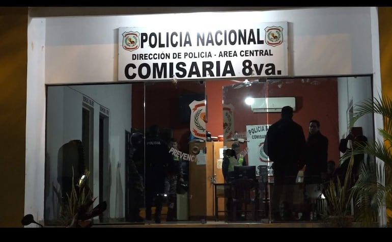 Varios agentes de policía en uniforme conversan al frente de la Comisaría Octava Central, con escritorio y computadora visibles.