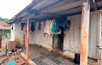 Estructura de vivienda rural con paredes de madera desgastada y prendas colgadas, sin personas visibles en el entorno.