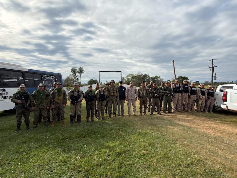 Veinte personas con vestimenta de camuflaje forman un grupo, algunas portan armas, en un entorno natural bajo un cielo nublado.