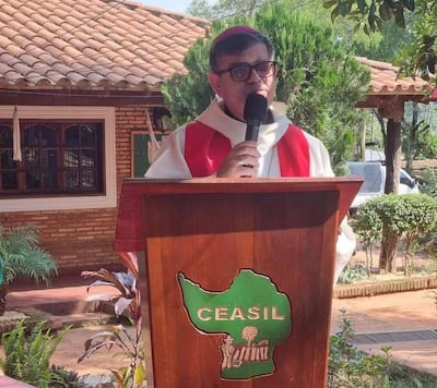 Monseñor Osmar López en estola roja y túnica blanca, hablando desde un podio con logotipo de CEASIL en entorno natural.