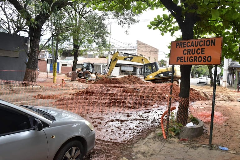 Zona de construcción con máquinas excavadoras CAT en terreno removido, malla de seguridad y letrero de advertencia de peligro.
