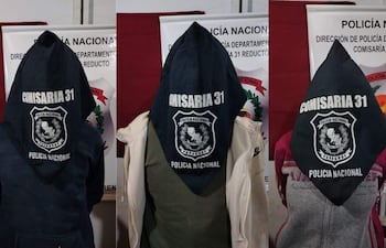 Tres personas de espaldas, vestidas con capuchones negros inscriptos con 'COMISARIA 31', en ambiente de la Policía Nacional.