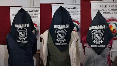 Tres personas de espaldas, vestidas con capuchones negros inscriptos con 'COMISARIA 31', en ambiente de la Policía Nacional.
