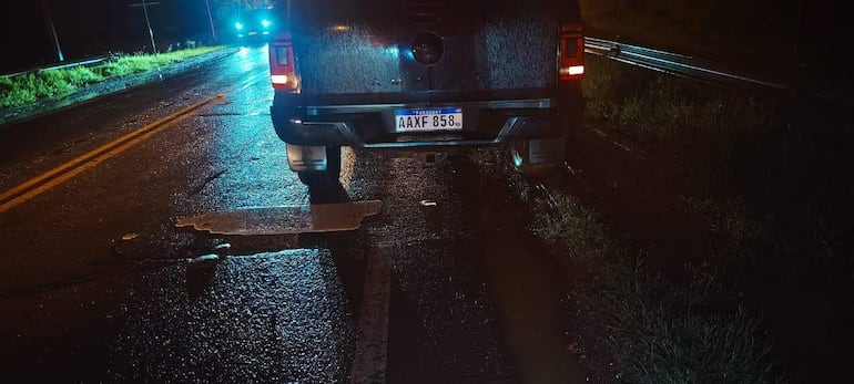 Camioneta oscura estacionada con luces de emergencia, carretera mojada y matrícula visible 'AAXF 858'.