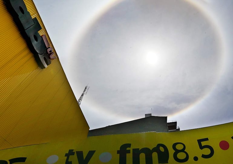 Cielo nublado de Asunción con un halo solar brillante alrededor del sol, y un edificio con la inscripción 'ABC' en primer plano.
