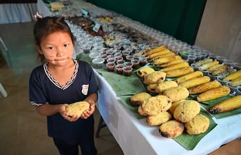 Niña con líneas pintadas en el rostro, camiseta oscura, sosteniendo galleta, frente a mesa con comida en feria gastronómica.