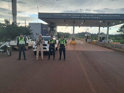 Cuatro hombres uniformados con chalecos reflectantes y armas, controlan la seguridad en el peaje de Mayor Otaño bajo un cielo nublado.