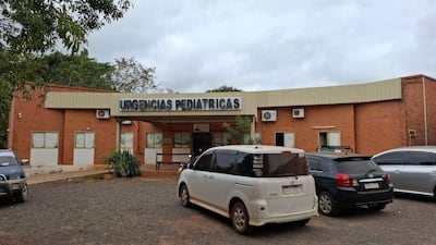 Fachada del hospital con letrero 'URGENCIAS PEDIÁTRICAS', vehículos estacionados y clima nublado.