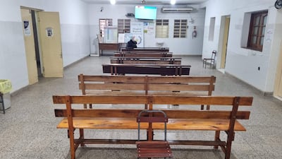 Sala de espera del hospital con bancos de madera vacíos y una persona sentada al fondo, ambiente tranquilo