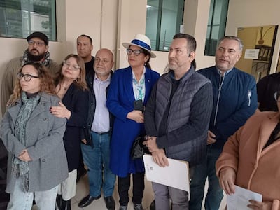 Grupo de siete personas, una mujer con chaqueta azul y sombrero blanco, sostiene un móvil mientras los demás la escuchan atentamente.