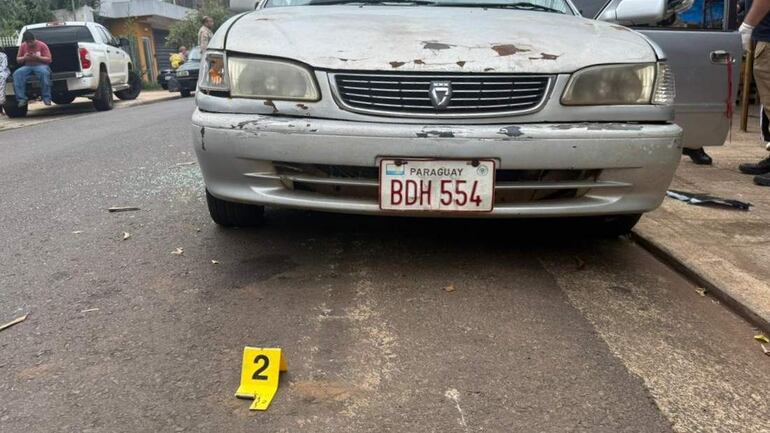 Vehículo sedán plateado descascarado en una calle, con etiqueta amarilla '2' que sugiere investigación criminal.