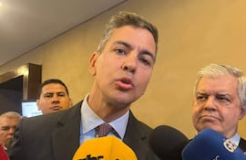 Enrique Riera Escudero en traje oscuro, habla con micrófonos a su alrededor, mientras Santiago Peña lo escucha atentamente.