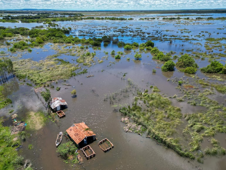 Paisaje inundado con vegetación y estructuras deterioradas, sin personas visibles y bajo un cielo soleado.