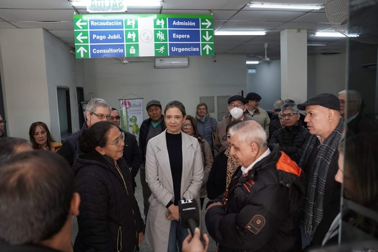Isaías Fretes en chaqueta oscura, conversando con mujer de chaqueta clara, rodeados de ciudadanos en un centro de salud.