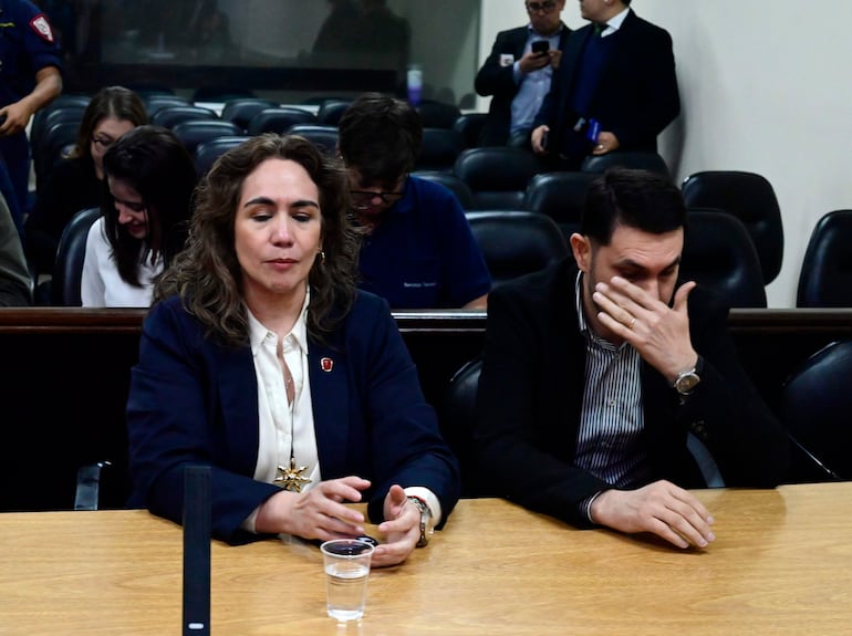 Alba Zaracho con chaqueta oscura y blusa blanca, mirando reflexiva a Hernán Rivas, que se cubre el rostro con la mano.