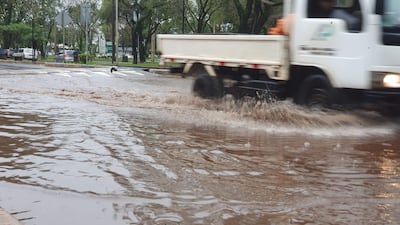 Camioneta blanca en movimiento sobre calle inundada en área urbana con vegetación alrededor.