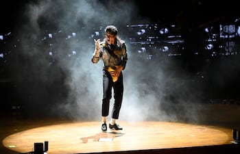 Michael Jackson en escenario circular iluminado, vestido con chaqueta brillante y pantalones negros, en movimiento en un concierto.