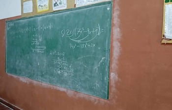 Aula con pizarrón verde y ejercicios matemáticos escritos, paredes terracota y carteles decorativos en alto.