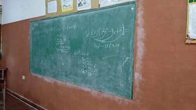 Aula con pizarrón verde y ejercicios matemáticos escritos, paredes terracota y carteles decorativos en alto.