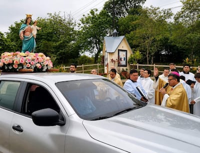 Monseñor López Benítez en túnica dorada, rodeado de hombres con túnicas blancas, bendiciendo la Virgen decorada con flores.