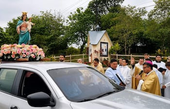 Monseñor López Benítez en túnica dorada, rodeado de hombres con túnicas blancas, bendiciendo la Virgen decorada con flores.
