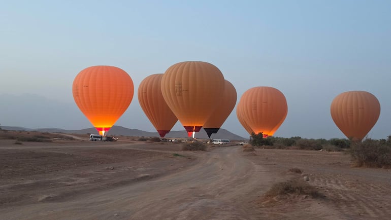 Globos aerostáticos naranjas brillantes flotan en un cielo despejado sobre un terreno desértico en Jbilet, Marruecos.