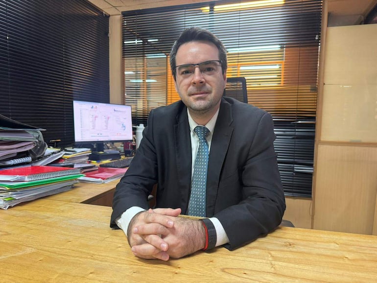 Marcelo Benítez en traje oscuro con corbata de puntos, sentado frente a una computadora, en un entorno de oficina.