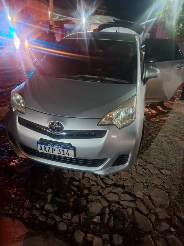Automóvil plateado Toyota con matrícula AAZP 314, luces de emergencia activadas en un entorno urbano nocturno.