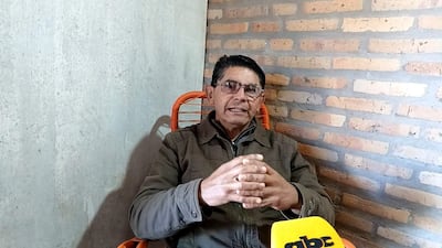 Roberto Ayal, hombre canoso con gafas y chaqueta gris, enfatiza su discurso sentado ante un micrófono en una habitación sencilla.