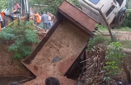 Dos adolescentes con camisetas, observan un camión volcado en terreno rural, rodeado de trabajadores y maquinaria.