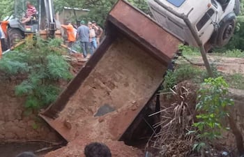 Dos adolescentes con camisetas, observan un camión volcado en terreno rural, rodeado de trabajadores y maquinaria.