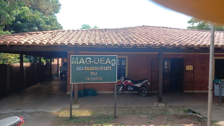 Edificio del MAG con letrero visible, rodeado de vegetación y dos motos estacionadas, en ambiente tranquilo.